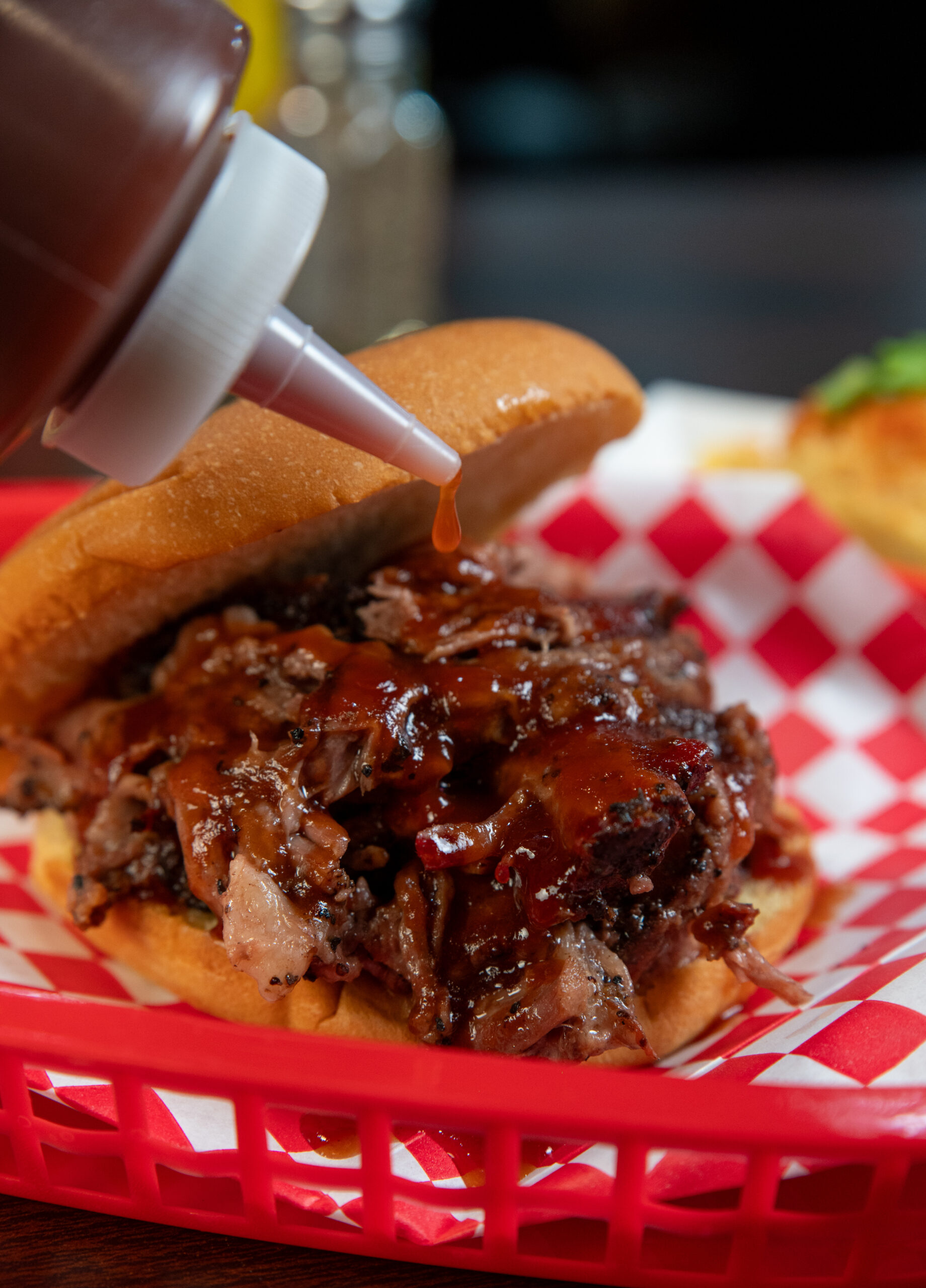 BrisketSandwich-OKSmokeBBQ - Oklahoma Smoke BBQ Pouring BBQ sauce on a brisket sandwich.