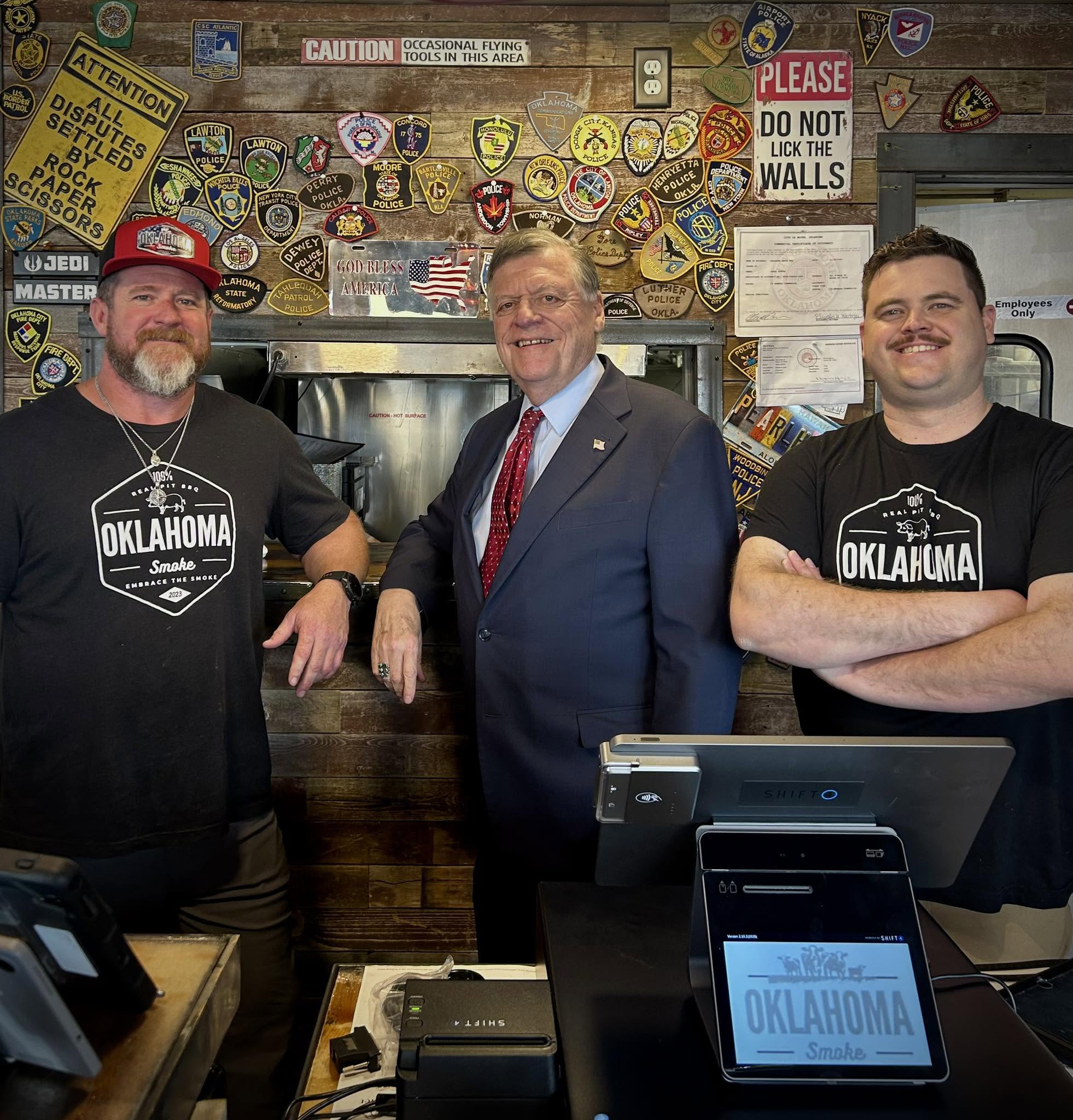 Three guys taking a picture of behind the counter of Oklahoma Smoke BBQ.