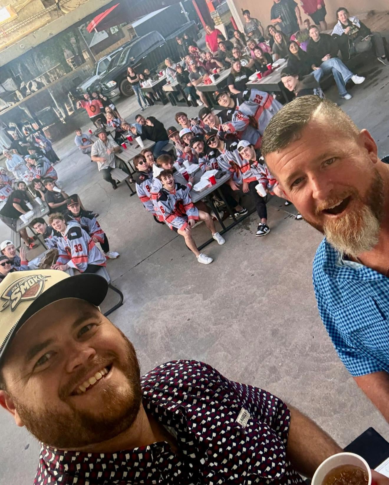 Founders of Oklahoma Smoke BBQ taking a picture with a whole hocky team eating catering.
