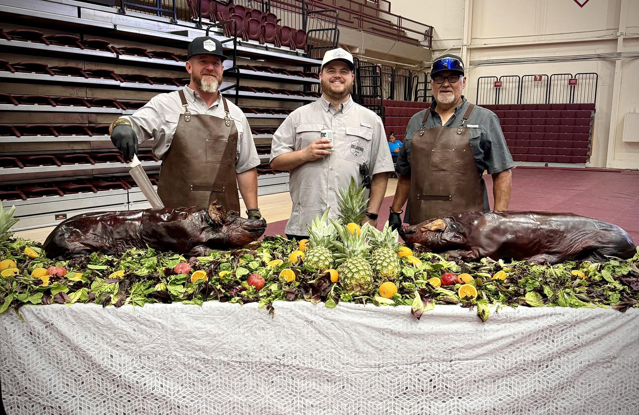 The three founders standing behind smoked pigs.